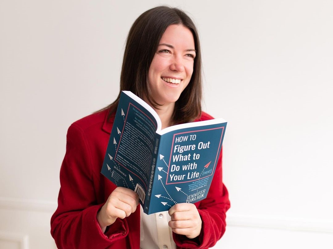 Head and shoulder photo of Jennifer Turliuk, wearing a red jacket with a white shirt and holding her book How to Figure out What to do with Your Life (next).